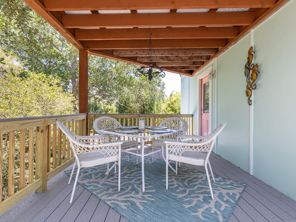 A covered outdoor patio with a wooden deck, white wicker furniture, and a patterned rug.