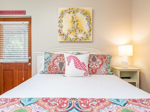 A bed with a colorful bedspread, patterned pillows, a wall art piece, and a bedside lamp. - Treetop Cottage by Tybee Vacation Rentals (Tybee Island)