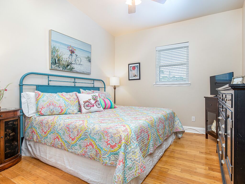 A bedroom with a bed, a nightstand, a dresser, a painting, and a window.