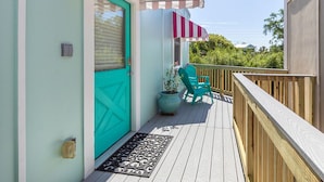 A wooden deck with a turquoise door, a potted plant, and a chair. - Treetop Cottage by Tybee Vacation Rentals (Tybee Island)