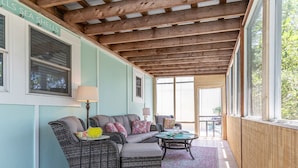 A covered patio area with wicker furniture, a table, and a view of the sea. - Treetop Cottage by Tybee Vacation Rentals (Tybee Island)
