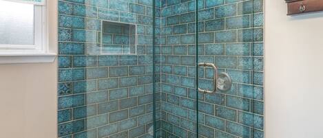 A shower with blue mosaic tiles and a glass door.