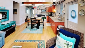 A cozy living room with a blue sofa, a dining area with wooden chairs, and a kitchen with wooden cabinets and a microwave. - Treetop Cottage by Tybee Vacation Rentals (Tybee Island)