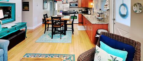 A cozy living room with a blue sofa, a dining area with wooden chairs, and a kitchen with wooden cabinets and a microwave.