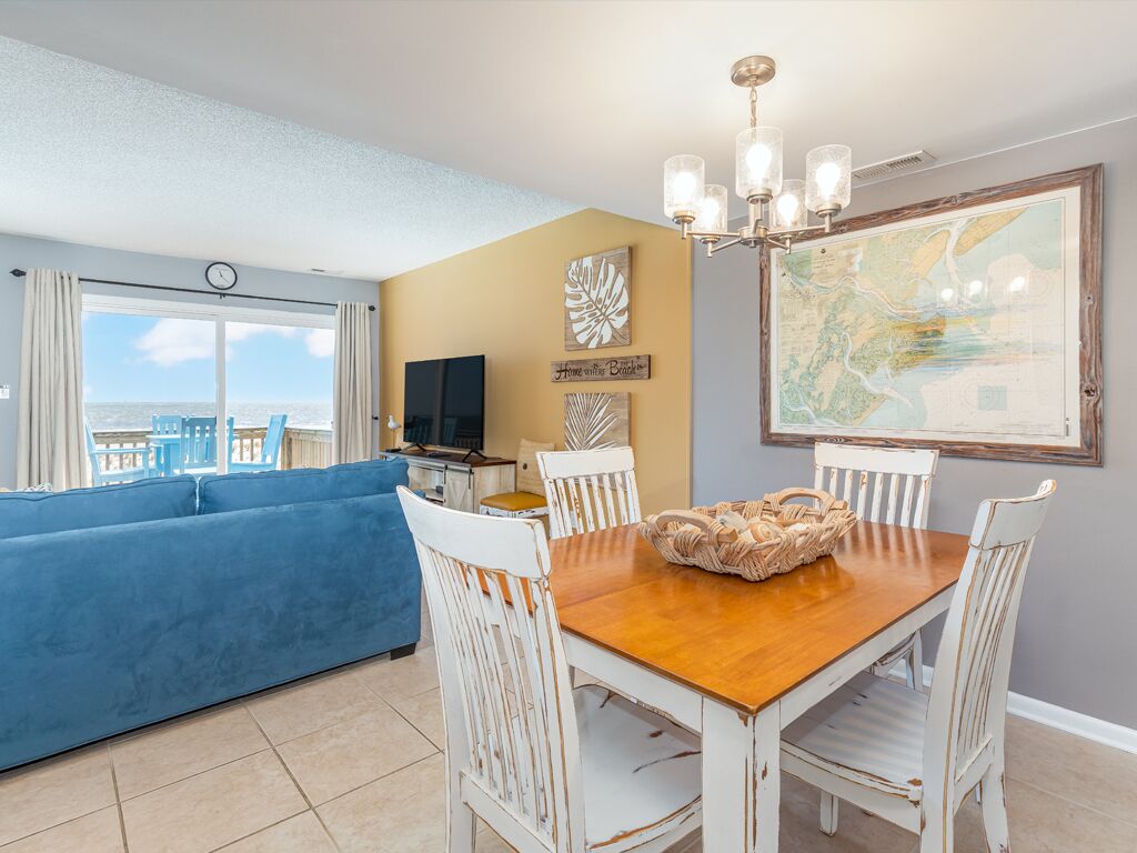 A living room with a blue sofa, a wooden dining table with white chairs, a chandelier, and a large map on the wall.