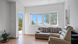 A spacious living room with a beige sofa, a small potted plant, and a window with a view of trees and a clear sky. - Cozy apartment in Murter with kitchen (Murter)