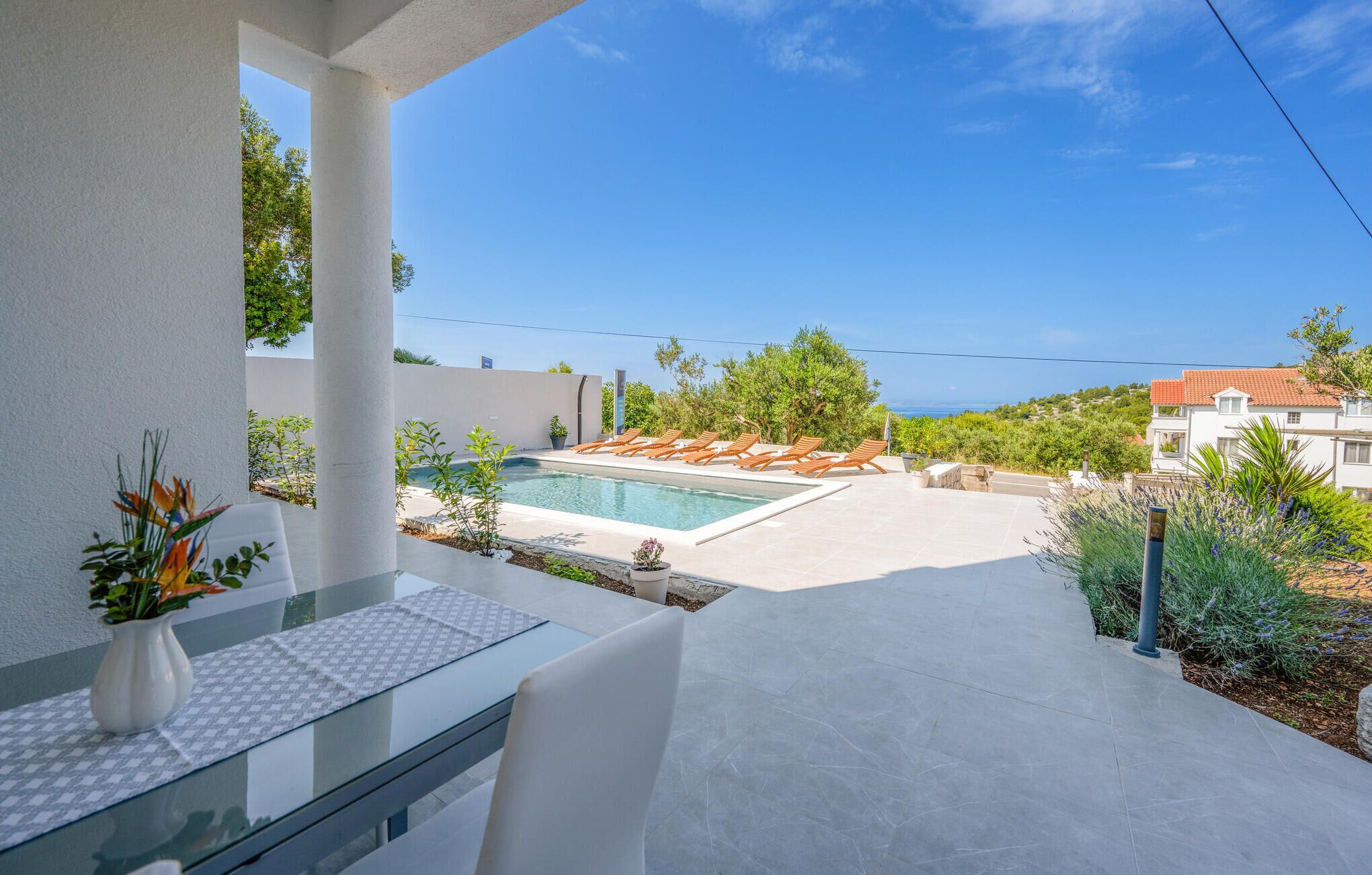 Un espace piscine extérieur moderne, doté de chaises longues, d’une table en verre et offrant une vue sur la mer.