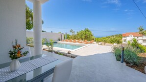 A modern outdoor pool area with lounge chairs, a glass table, and a view of the sea. - Cozy apartment in Murter with kitchen (Murter)