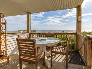 Relax in this serene beachside seating area with a round table and comfortable chairs, surrounded by a fence and offering a stunning ocean view.