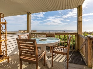 Relax in this serene beachside seating area with a round table and comfortable chairs, surrounded by a fence and offering a stunning ocean view.