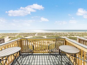 A wooden deck with two round tables and chairs, overlooking a beach with dunes and the ocean. - Tybee Lights 114C by Tybee Vacation Rentals (Tybee Island)