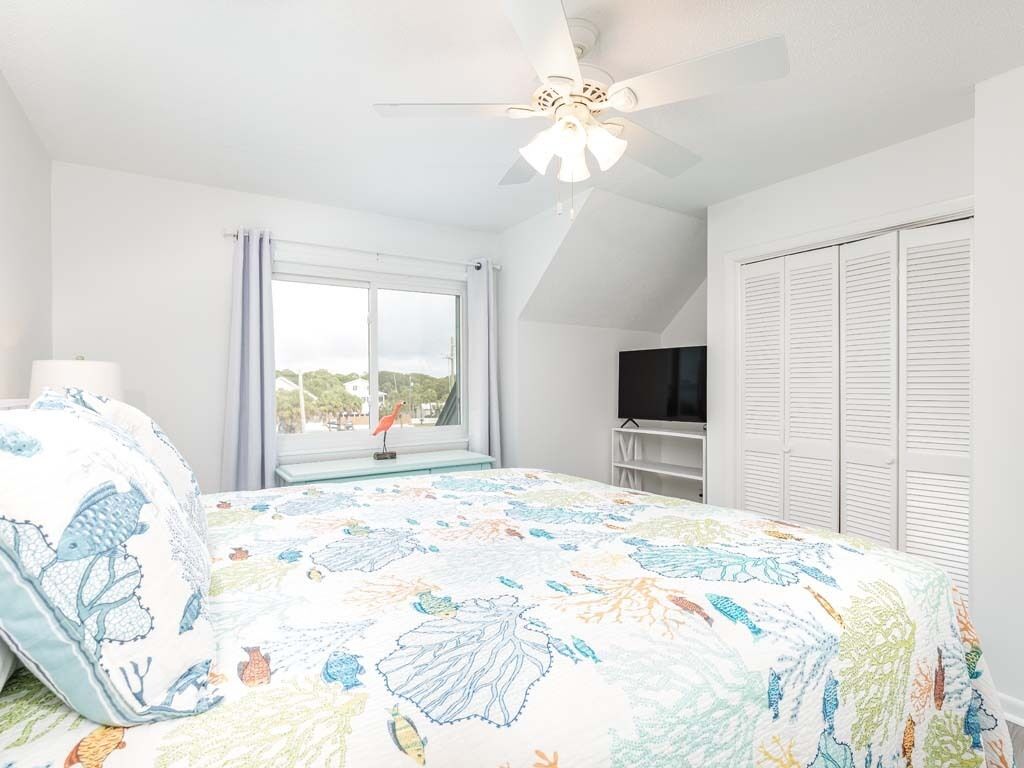 Un dormitorio con cama, ventilador de techo, ventana con cortinas, televisión y armario.