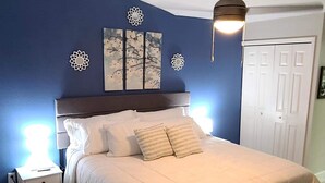A bedroom with a bed, a nightstand, a ceiling fan, and decorative wall art. - Charming Villa in Safety Harbor for the Family (Safety Harbor)