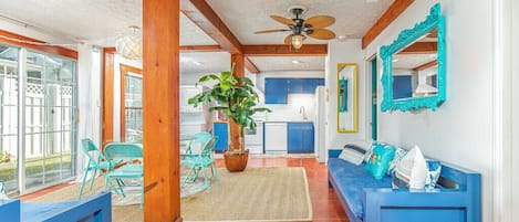 A spacious living area with a blue sofa, a blue bench, and a ceiling fan. There is a large window providing natural light and a view of the outside.