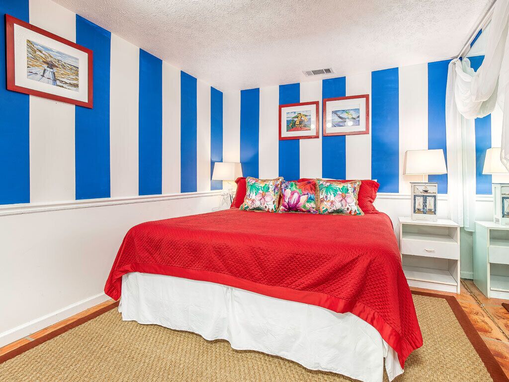 Een slaapkamer met een bed, gestreepte wanden en twee nachtkastjes met lampen.