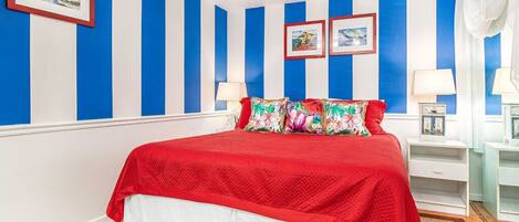 Een slaapkamer met een bed, gestreepte wanden en twee nachtkastjes met lampen.