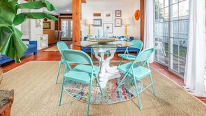 A dining area with a round table and turquoise chairs, surrounded by large windows and a view of the outdoors. - Tybreeza A by Tybee Vacation Rentals (Tybee Island)