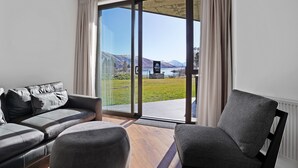 Een moderne woonkamer met een bank en fauteuils, een schuifdeur naar een balkon met uitzicht op bergen.