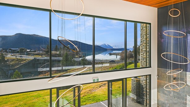 Een modern interieur met grote ramen, met uitzicht op een bergachtig landschap en een brug.