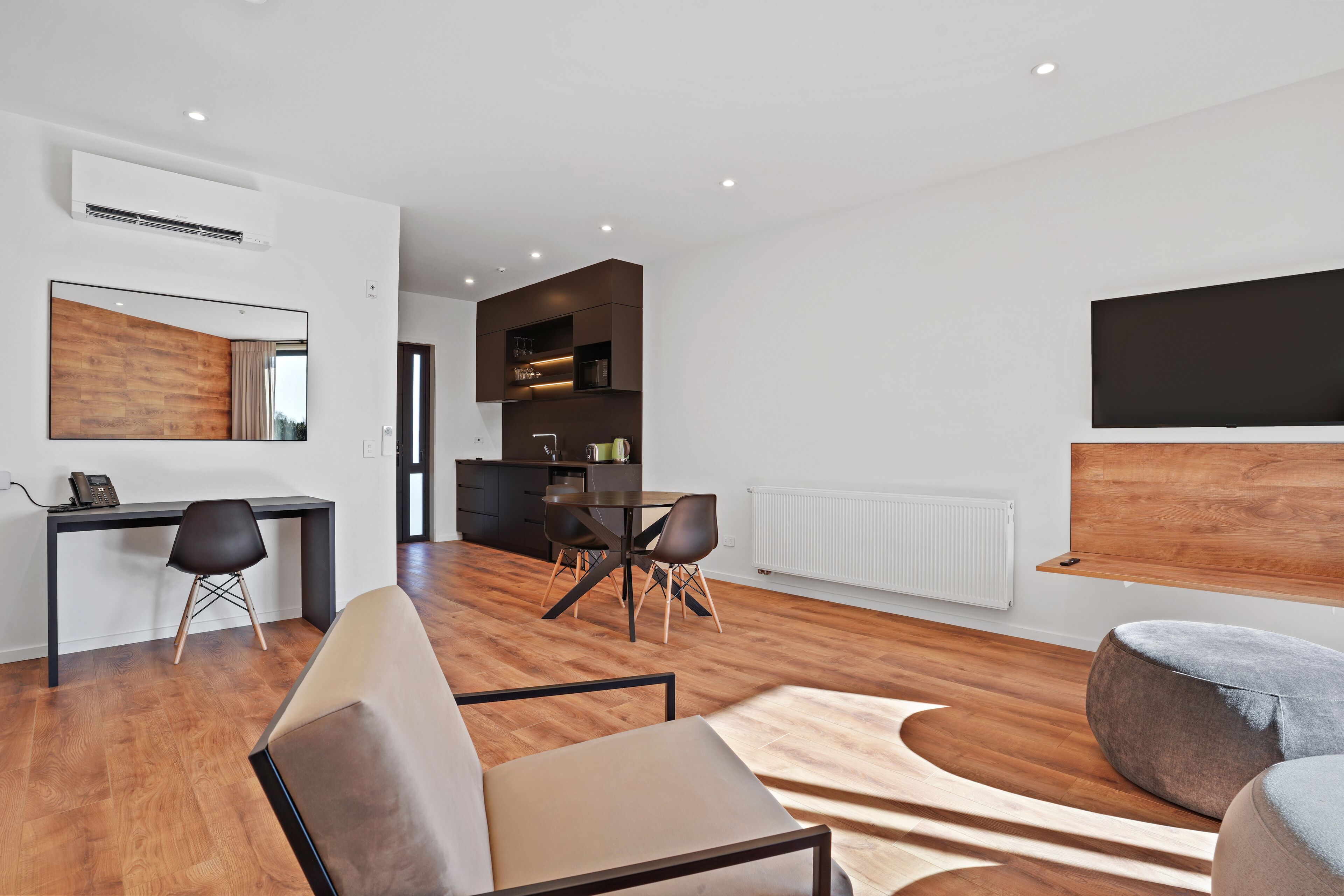 Una sala de estar moderna con piso de madera, un sofá, una mesa de comedor con sillas, una zona de cocina y un espejo grande.