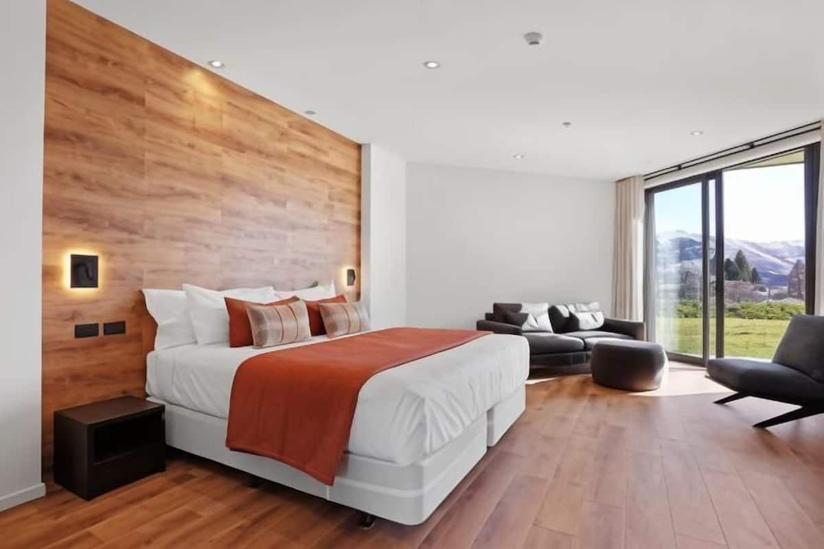 Ein modernes Schlafzimmer mit einem großen Bett, einer Wand als Holzdekor, einer Couch und Blick auf Berge.