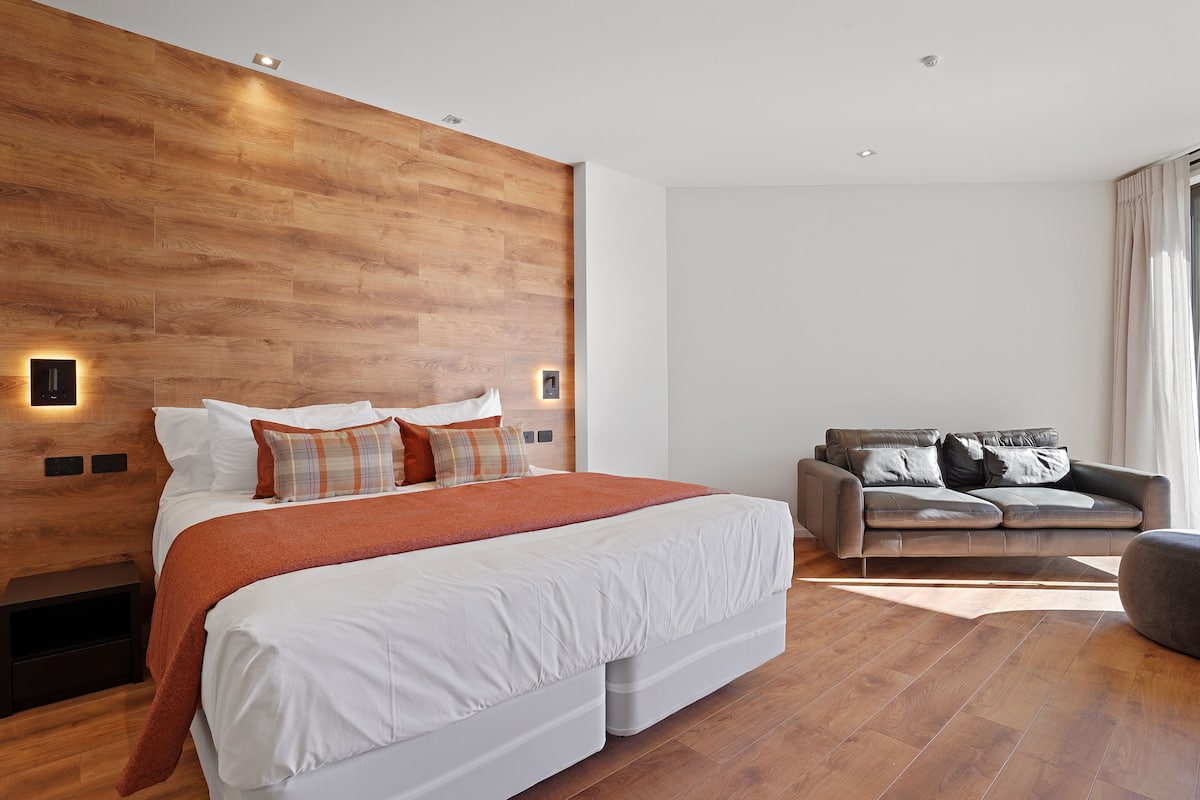 Ein modernes Schlafzimmer mit einem großen Bett, einer Couch und Holzvertäfelung an der Wand.
