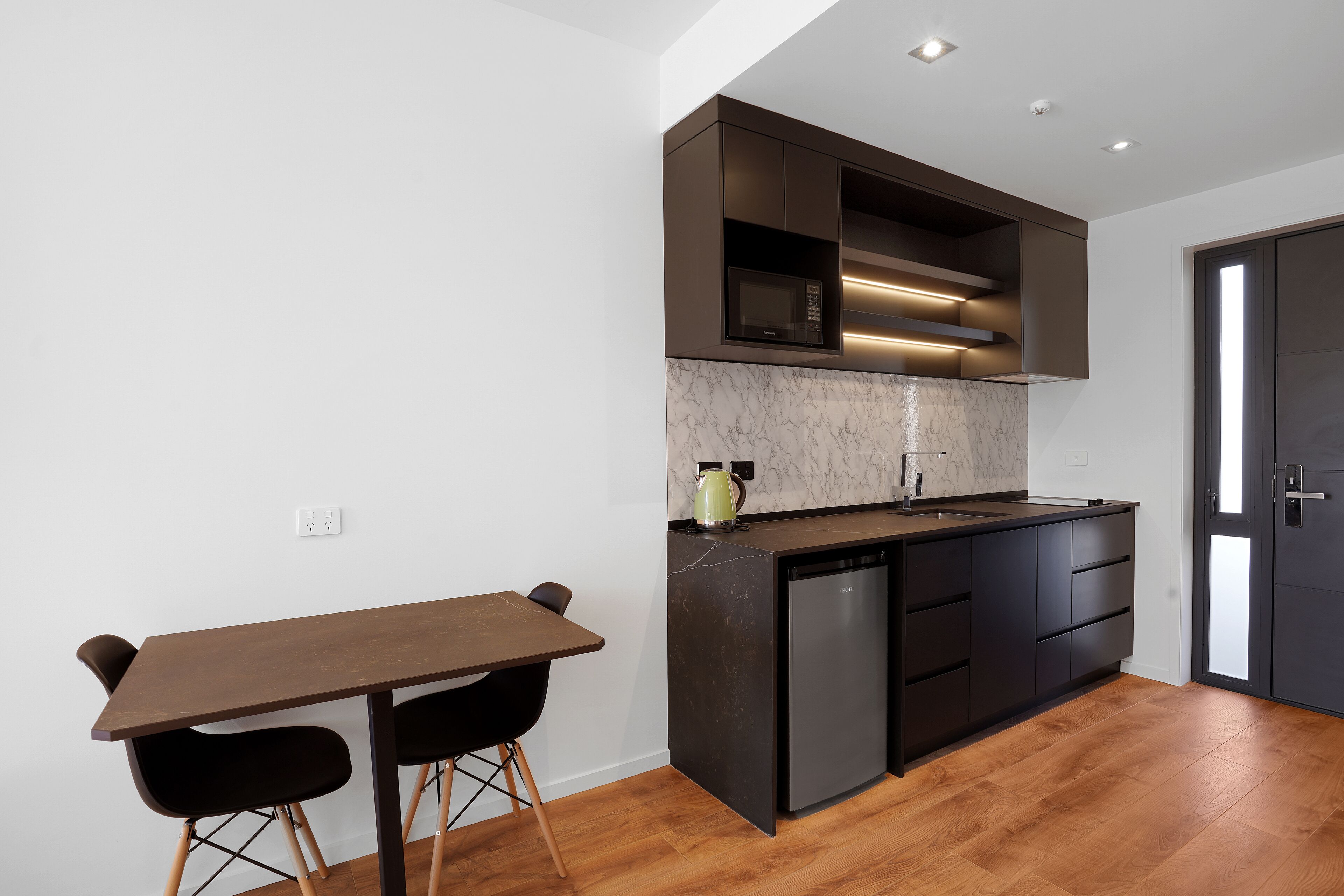 A modern kitchen with dark cabinetry, a marble countertop, and a built-in dishwasher.