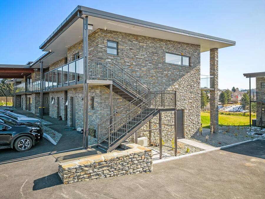 Un edificio moderno con fachada de piedra, una escalera y un área exterior cubierta.