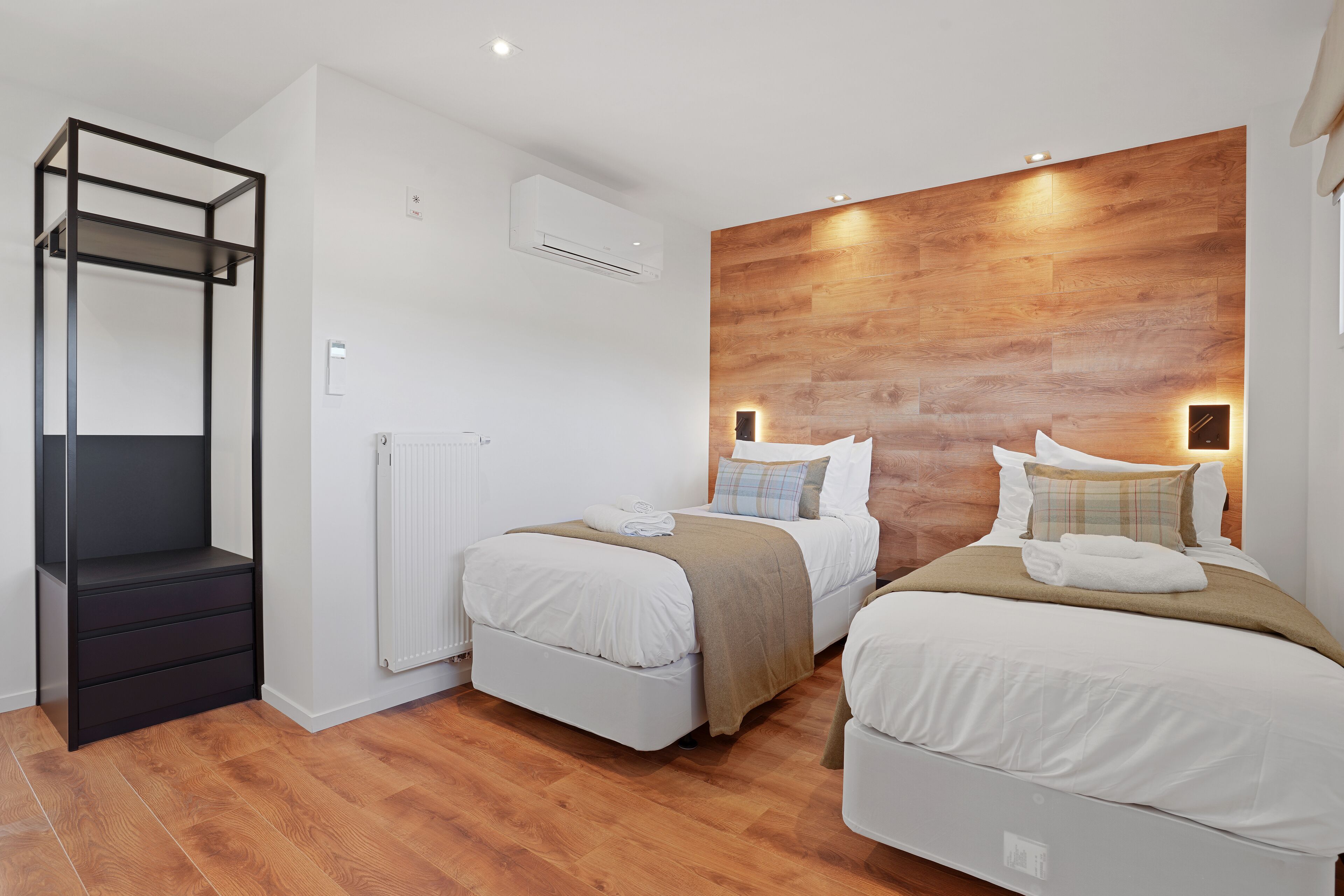 A modern bedroom with two beds, a built-in wardrobe, and a wooden accent wall.