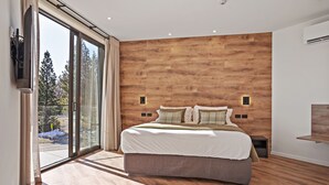 Een moderne slaapkamer met een groot bed, houten wandbekleding, een schuifglazen deur naar buiten en een tv aan de muur.