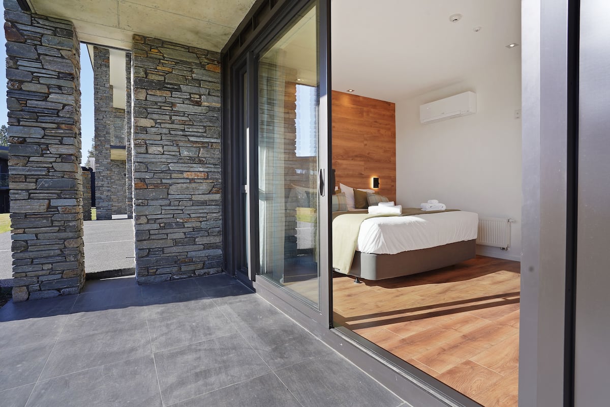 Ein modernes Schlafzimmer mit einer Steinwand, einer Glastür zum Balkon und Holzboden.