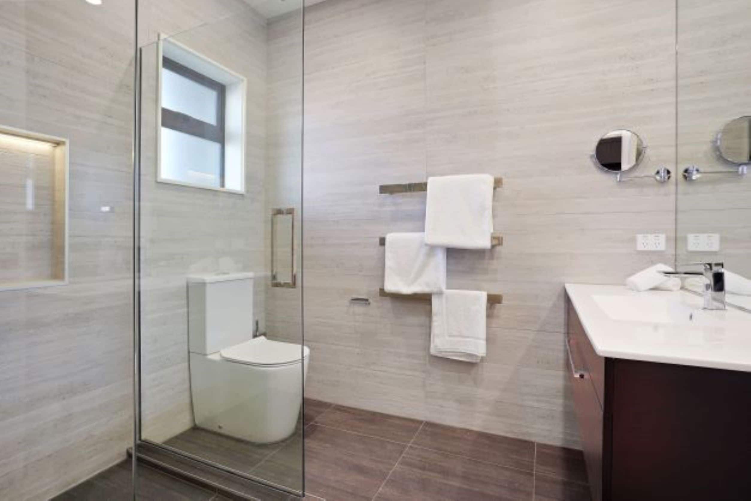 Une salle de bain moderne avec une douche à parois de verre, des toilettes, un meuble-lavabo avec un miroir et un porte-serviettes.