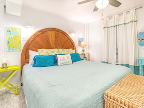 A bedroom with a large bed, a wooden headboard, a bedside table with a lamp, and a window with curtains.