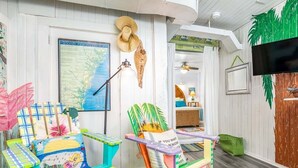 A room with a map of Coastal Georgia, a hat, a lamp, a TV, and colorful furniture. - Tybreeza B by Tybee Vacation Rentals (Tybee Island)