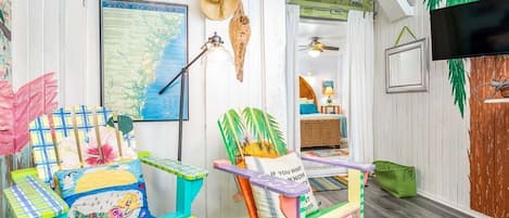 Una habitación con un mapa de la costa de Georgia, un sombrero, una lámpara, un televisor y muebles coloridos.