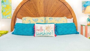 A bed with a wooden headboard, two pillows with a 'hello sunshine' design, and a blue blanket. - Tybreeza B by Tybee Vacation Rentals (Tybee Island)