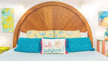 A bed with a wooden headboard, two pillows with a 'hello sunshine' design, and a blue blanket.
