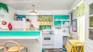 A compact kitchen with white cabinets, a teal countertop, and yellow chairs. - Tybreeza B by Tybee Vacation Rentals (Tybee Island)