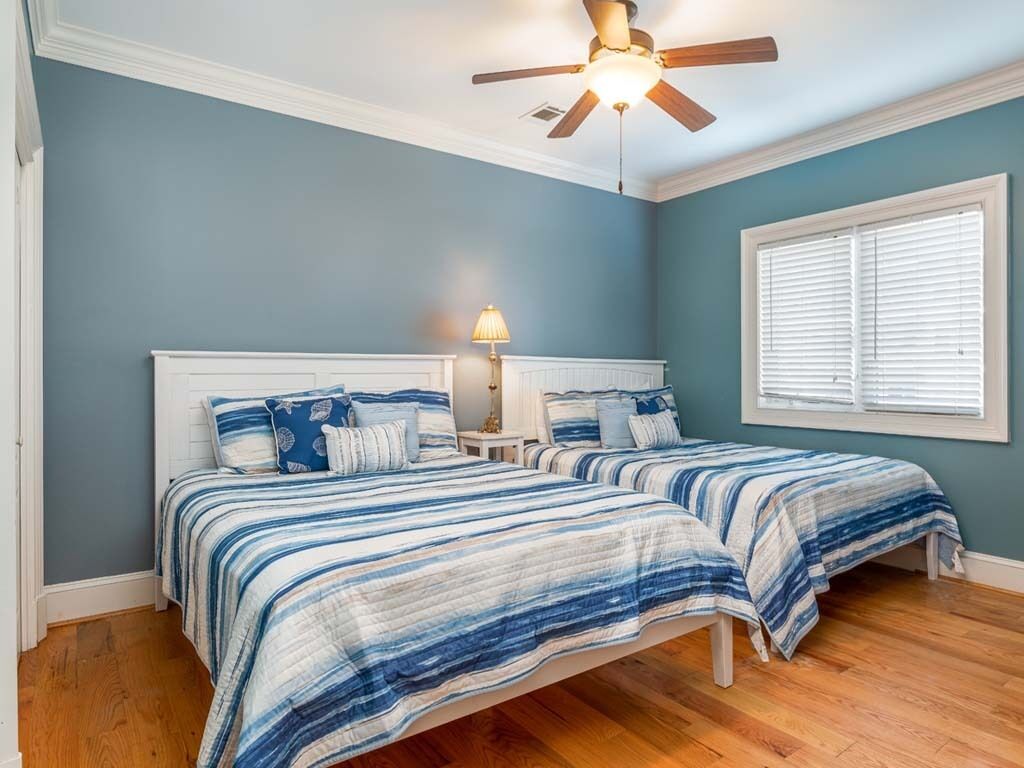 A bedroom with two beds, a ceiling fan, a bedside lamp, and a window with blinds.