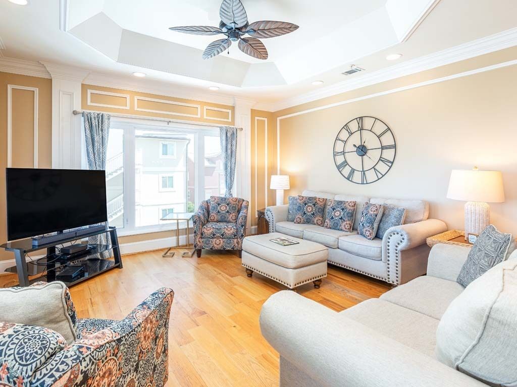 Ein Wohnzimmer mit großem Flachbildfernseher, Deckenventilator, einer Sofagarnitur und einer großen Wanduhr.