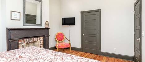 Un dormitorio con una cama, chimenea, televisor y dos puertas.