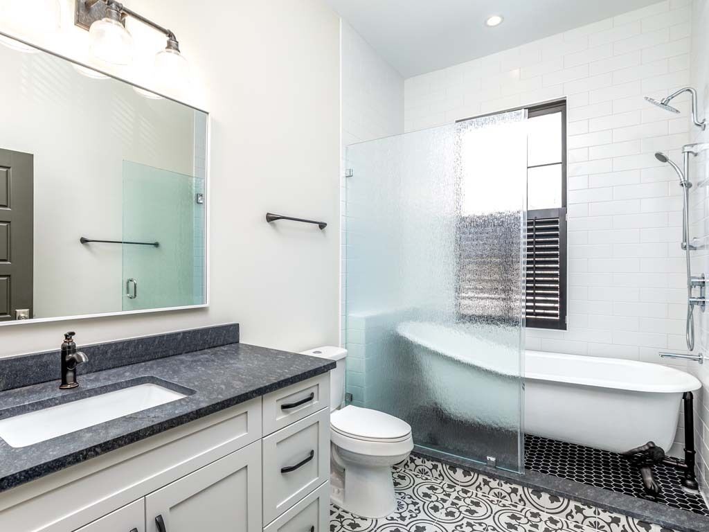 A modern bathroom with a glass-enclosed shower, a white bathtub, and a marble countertop sink.