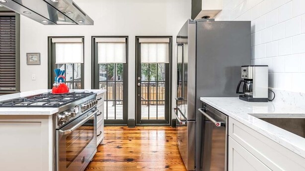 A modern kitchen with a central island, stainless steel appliances, and a view through glass doors to an outdoor deck. - Waldburg Terrace by Tybee Vacation Rentals (Savannah)