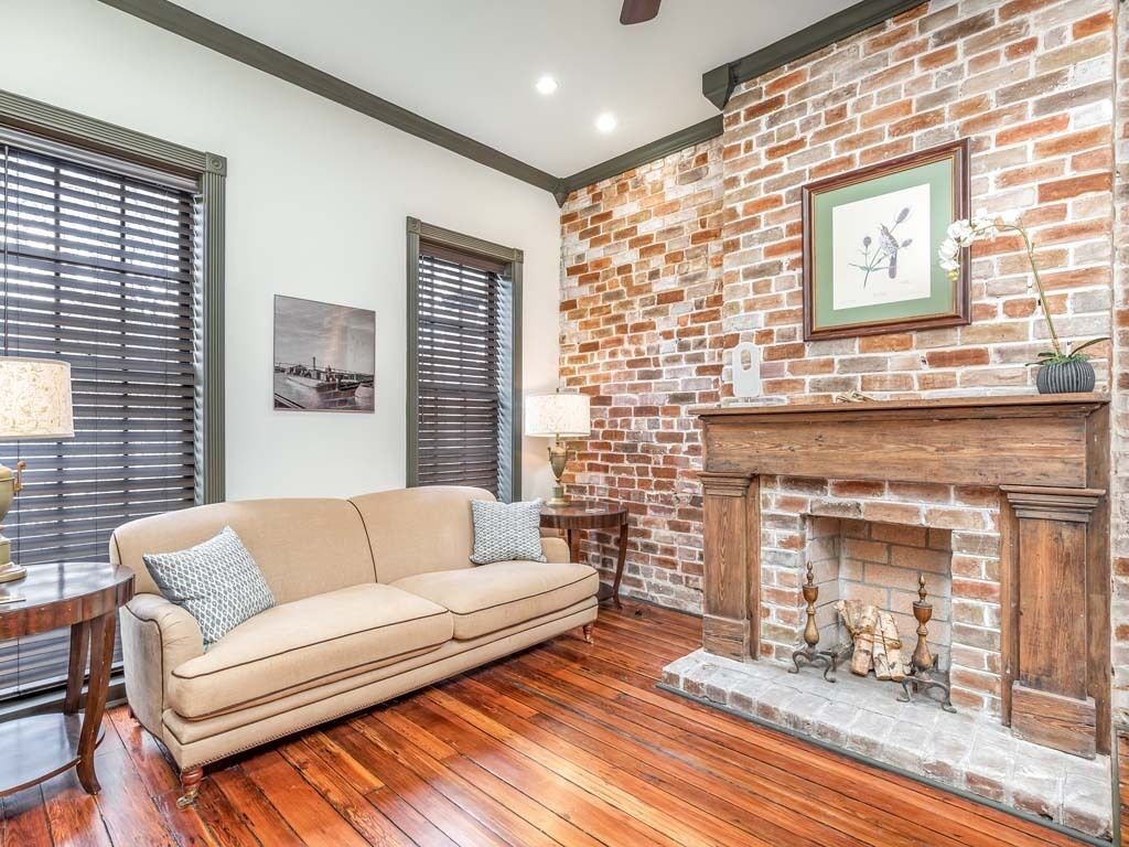 A living room with a brick fireplace, a beige sofa, and a wooden floor.
