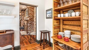 A cozy interior with a wooden floor, a brick wall, and a shelf with plates and glasses. - Waldburg Terrace by Tybee Vacation Rentals (Savannah)