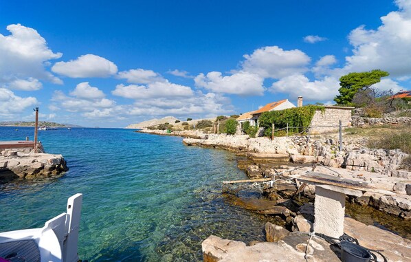 A coastal scene with clear waters, a stone pier, and a building with a tiled roof.