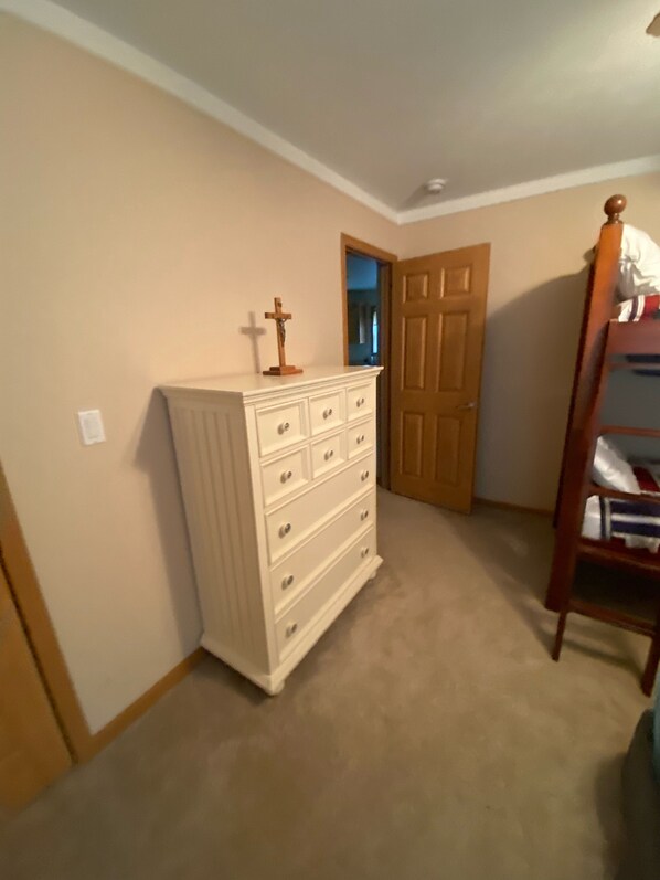 Une chambre avec une commode blanche, une porte en bois et un lit superposé.