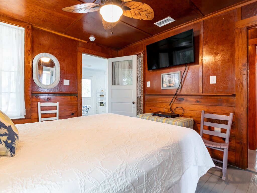 Ein Zimmer mit Holzboden, einem Bett, einem Fernseher, einem Spiegel und einer Tür.