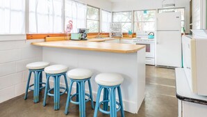 Une cuisine avec un îlot central en bois, des tabourets de bar blancs et des appareils électroménagers blancs.