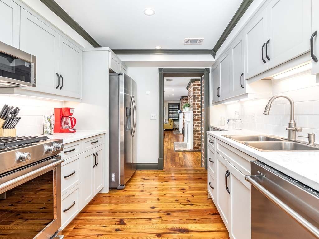 A modern kitchen with white cabinets, stainless steel appliances, and a wooden floor.